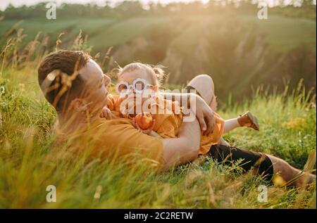 Young father lies in grass and hugs his daughter while walking in park. Stock Photo