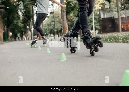 Roller skating, two skater rolling around the cones in park. Urban roller-skating, active extreme sport outdoors, youth leisure, rollerskating Stock Photo
