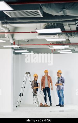 Vertical long shot of three professional construction engineers gathered together in unfinished room talking to each other, copy space Stock Photo