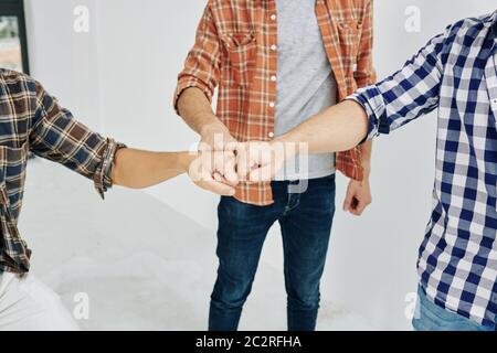 Three unrecognizable men wearing casual outfits with checked shirts bumping their fists in symbol of unity and friendship, high angle shot Stock Photo