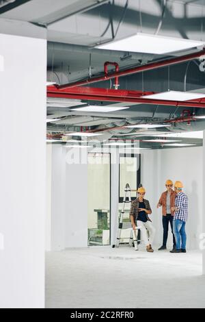 Long shot of three professional construction workers spending time in unfinished room having lively discussion, copy space Stock Photo