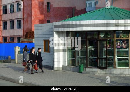 Pyongyang, North Korea - April 29, 2019: People in suburb of the city return home after work, carry shopping bags. Small street shop on the background Stock Photo