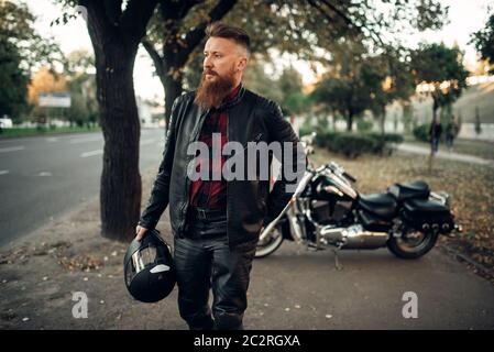 Bearded biker with helmet in hand in front of his chopper, back view. Vintage bike, road rider and his motorcycle, freedom lifestyle, biking Stock Photo