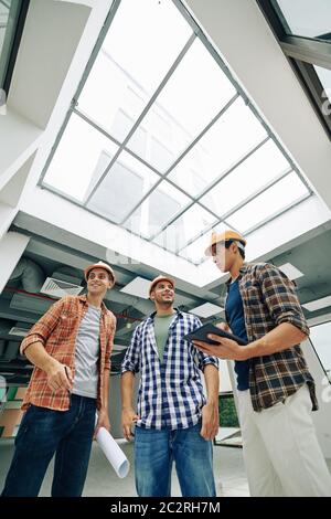 Vertical low angle view shot of joyful young construction engineers standing together talking about their work Stock Photo