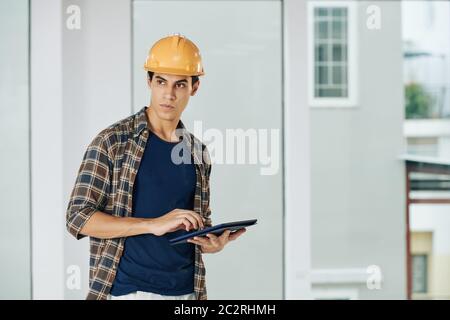 Horizontal medium shot of young engineer standing alone in empty room using tablet computer looking away, copy space Stock Photo
