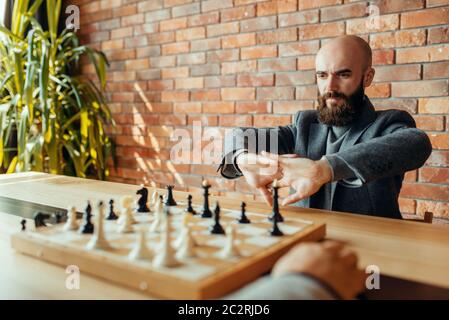 Male chess players on competition, board with figures. Two chessplayers begin the intellectual tournament indoors. Chessboard on wooden table, strateg Stock Photo