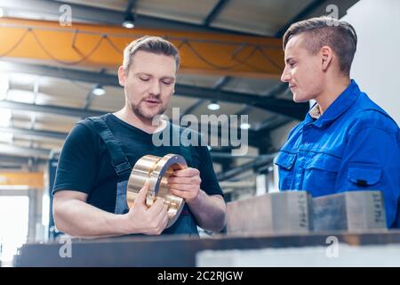 Skillful master discussing a workpiece with his apprentice or trainee Stock Photo