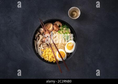 Ramen. Soba noodles with eggs, shiitake mushrooms, and vegetables, overhead shot on a black background with chopsticks and a cup Stock Photo