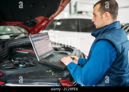 Engineer makes computer diagnostics of the car in auto-service. Vehicle wiring inspection Stock Photo