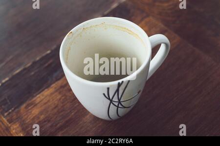 Old coffee in a ceramic mug sitting on a timber coffee table. Coffee stains on the inside of the mug Stock Photo