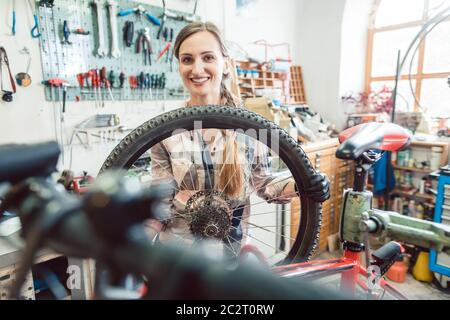 Very happy bike mechanic woman looking through the wheel of bicycle Stock Photo