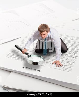 Man with big loupe sits on papers leaning on his palm and reading an agreement Stock Photo