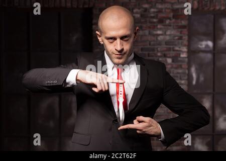 Silent assassin, oriental martial arts in action. Bald contract murderer in suit and red tie holds combat knife. Fighting knife is a dangerous weapon Stock Photo