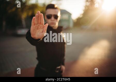 Serious police officer in uniform and sunglasses shows a hand stop sign, front view. Cop at the work. Law protection concept, safety control job Stock Photo