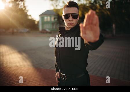 Serious police officer in uniform and sunglasses shows a hand stop sign, front view. Cop at the work. Law protection concept, safety control job Stock Photo