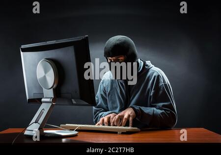 Hacker in balaclava mask stealing information in the office Stock Photo