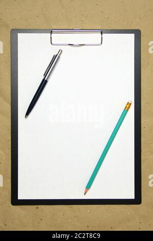 A tablet with a white sheet with pen and pencil on a beige craft paper. Concept of new opportunities, ideas, undertakings, innovations. Stock photo with empty place for your text and design. Stock Photo