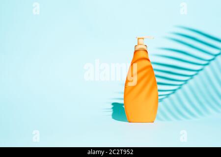 Orange container for lotion without label on blue background with leaf, space for text Stock Photo