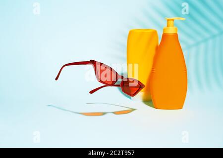 Two orange containers without label for lotion, flying sunglasses on blue background, space for text Stock Photo