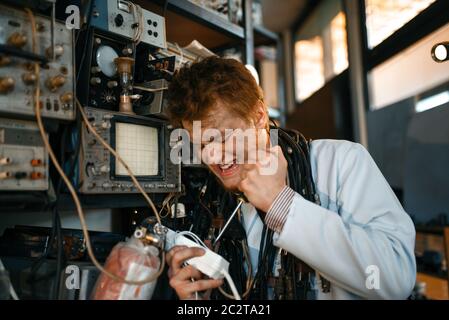 Crazy scientist works with electricity in laboratory. Electrical testing tools on background. Lab equipment, engineering workshop Stock Photo