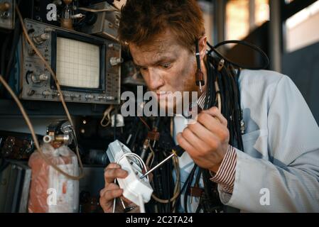 Crazy scientist works with electricity in laboratory. Electrical testing tools on background. Lab equipment, engineering workshop Stock Photo
