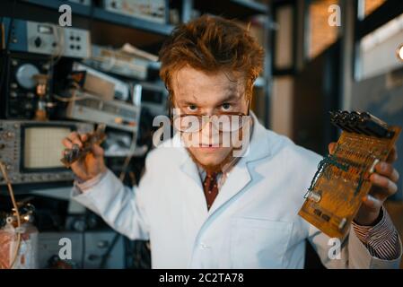 Strange engineer holds electric tube in laboratory. Electrical testing tools on background. Lab equipment, engineering workshop Stock Photo