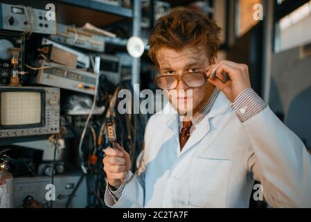 Strange engineer holds electric tube in laboratory. Electrical testing tools on background. Lab equipment, engineering workshop Stock Photo