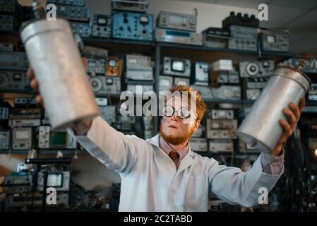 Strange scientist holds radiation devices in his hands, dangerous test in laboratory. Electrical testing tools on background. Lab equipment, engineeri Stock Photo