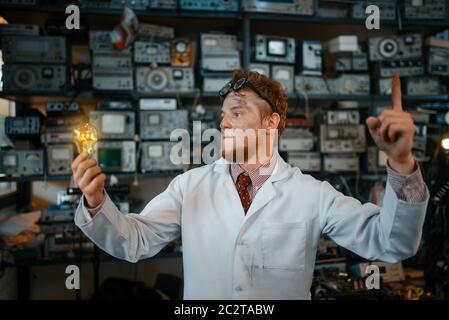 Strange scientist with a burning light in his hands, test in laboratory. Electrical testing tools on background. Lab equipment, engineering workshop Stock Photo