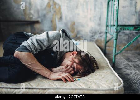 Male druggy with syringe in hand sleeping in bed after dose. Drug