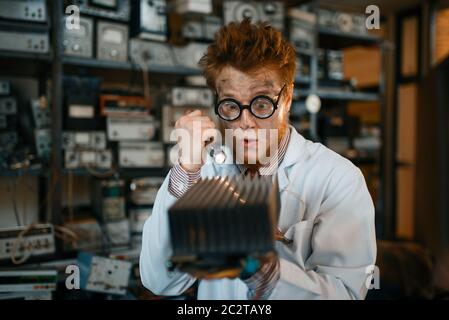Strange engineer examines the cooling radiator, test in laboratory. Electrical testing tools on background. Lab equipment, engineering workshop Stock Photo