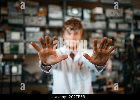 Strange scientist showing scorched hands in laboratory. Electrical testing tools on background. Lab equipment, engineering workshop Stock Photo