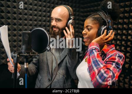 Male and female singers in headphones songs in audio recording studio. Musicians on record, professional music mixing Stock Photo