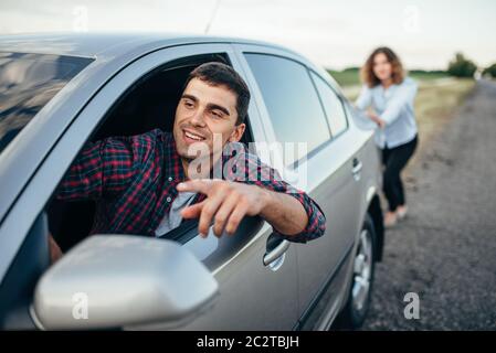 Woman pushing a broken car down the road, smiling man driver. Vehicle with trouble Stock Photo