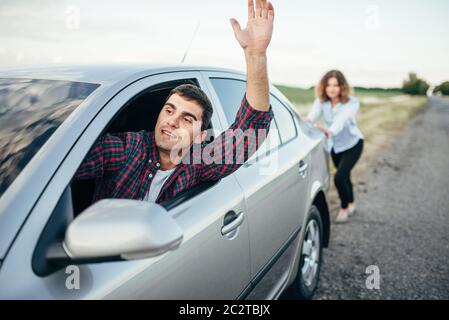Woman pushing a broken car down the road, smiling man driver. Vehicle with trouble Stock Photo