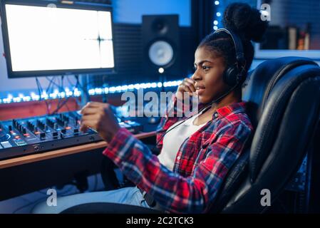 Female performer in headphones at the monitor in audio recording studio. Sound engineer at the mixer, professional music mixing Stock Photo