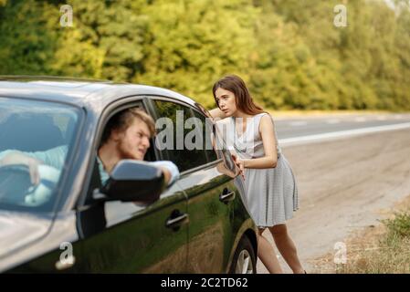 Young woman pushing broken car with man on road, breakdown. Crashed automobile or emergency accident with vehicle, trouble with engine on highway Stock Photo