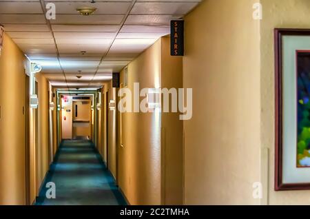 A view of the long hotel corridor, illuminated by a number of lights. Signs for exit and stairs are visible. Stock Photo