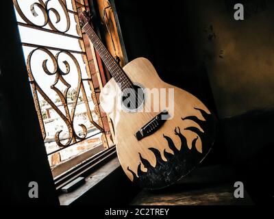 An acoustic guitar placed next to the old vintage window with soft sunlight coming from. Nostalgia guitar chords. Summer melody background. Close up. Stock Photo