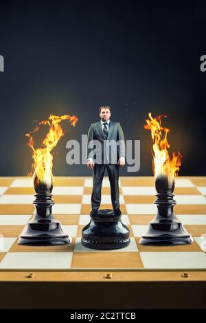 Businessman standing on the chess board instead of a pawn between two blames Stock Photo