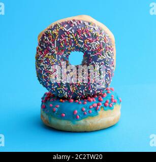 two round baked donut with colored sugar sprinkles and with blue sugar icing on a blue background Stock Photo