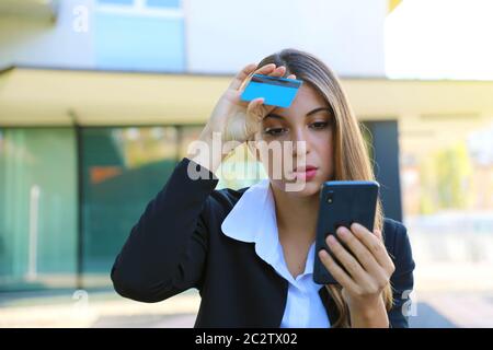 Desperate business woman looking on mobile phone her credit card statement stressed. Credit card cloned concept. Stock Photo