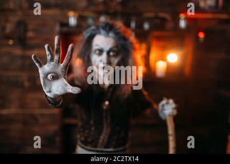 Scary witch with an eye in the palm reads mystic spell, spiritual seance. Female foreteller calls the spirits, terrible fortune teller Stock Photo