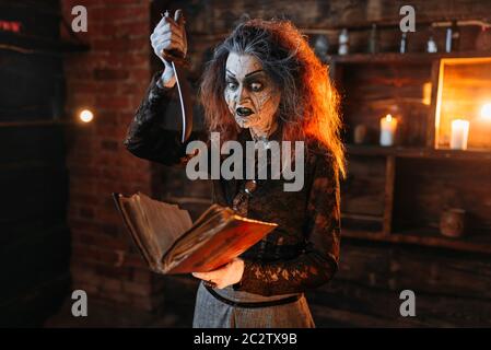 Scary witch holds spellbook and knife, dark powers of witchcraft, spiritual seance. Female foreteller calls the spirits, terrible future teller Stock Photo