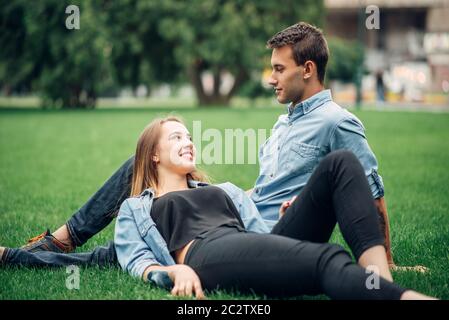 Phone addicted people, man and woman lies on the grass in summer park and using their smartphones, social addict Stock Photo