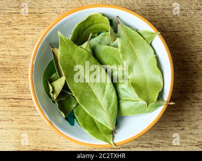 A small bowl of dried bay leaves centred on a wooden chopping board Stock Photo