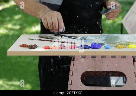 A painter using paint utensils (oil paint, artist brush and a palette knife) Stock Photo