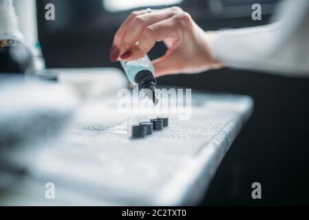 Female tattooist hands in blue sterile gloves holds tattoo machine, professional work tools on background. Tattooing in salon Stock Photo