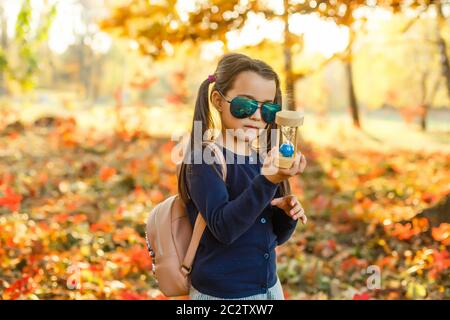 little girl with hourglass surrounded by autumn foliage Stock Photo