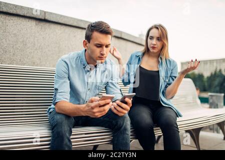 Phone addict man with two gadgets ignoring his woman. Social addicted people, problems in relationships Stock Photo